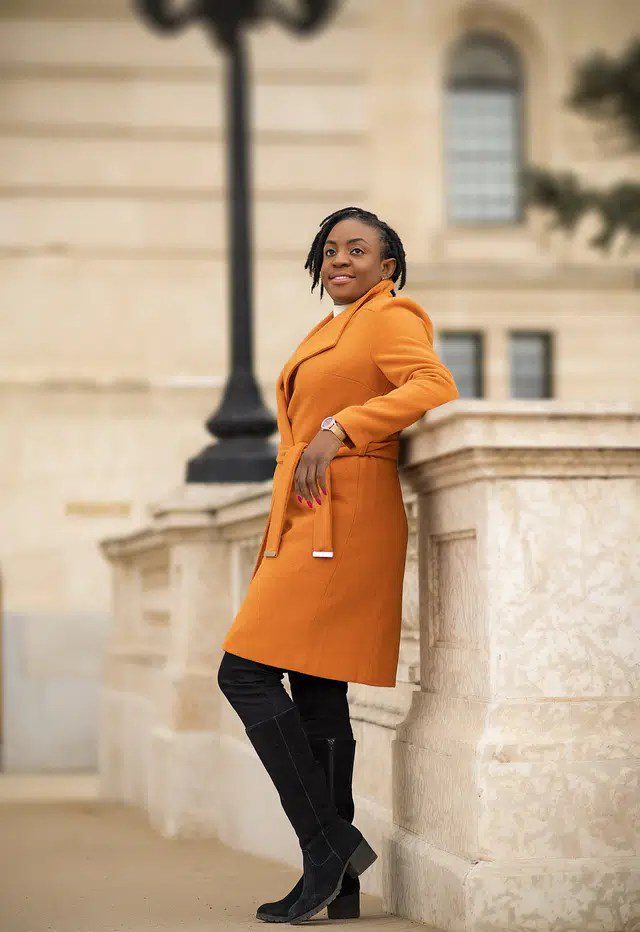 Young Woman Standing by a Wall Wearing an Orange Coat and Black Shoes